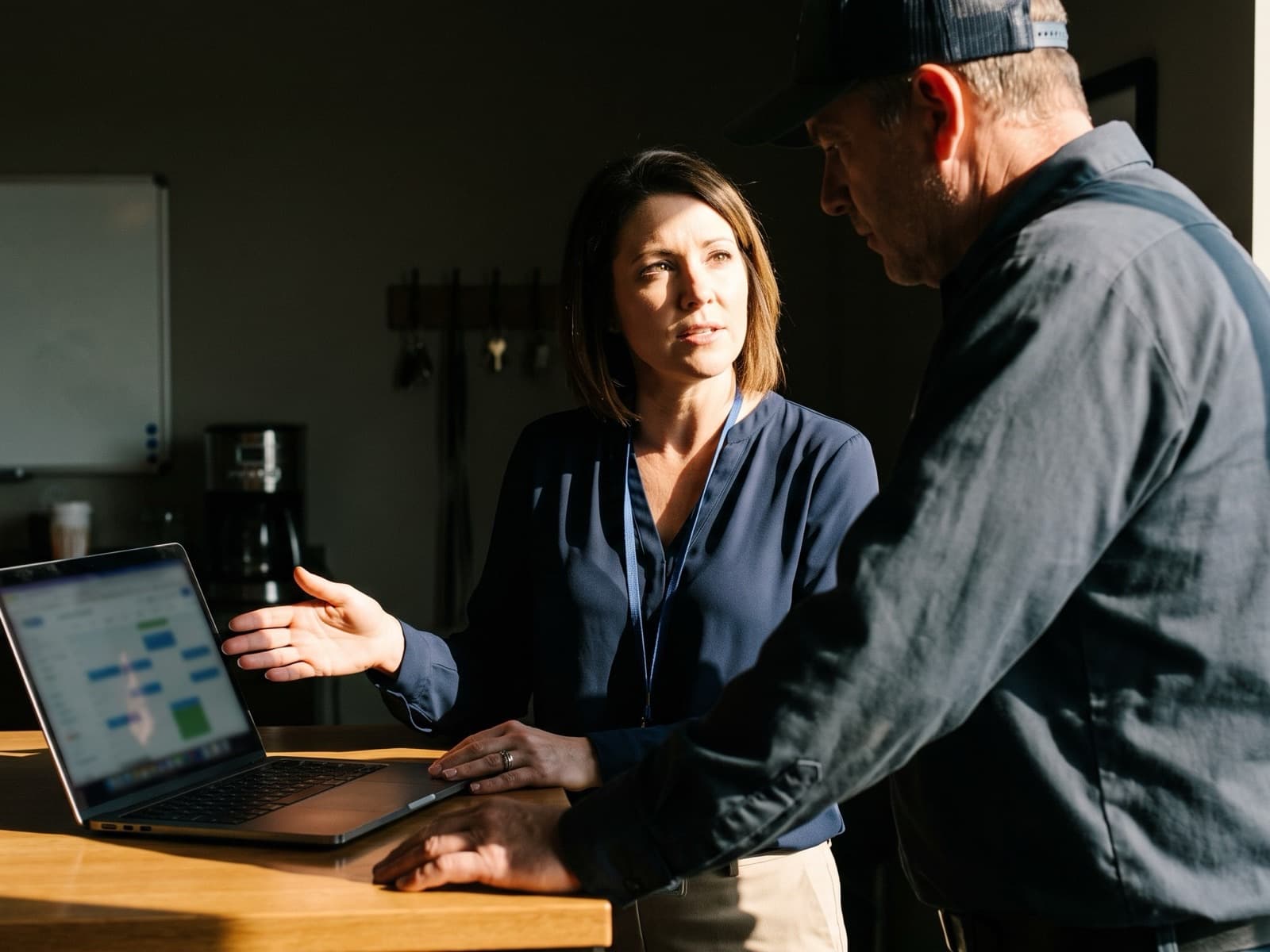 A referral partner at a home-services company's front-office counter showing the owner a scheduling dashboard on her laptop.